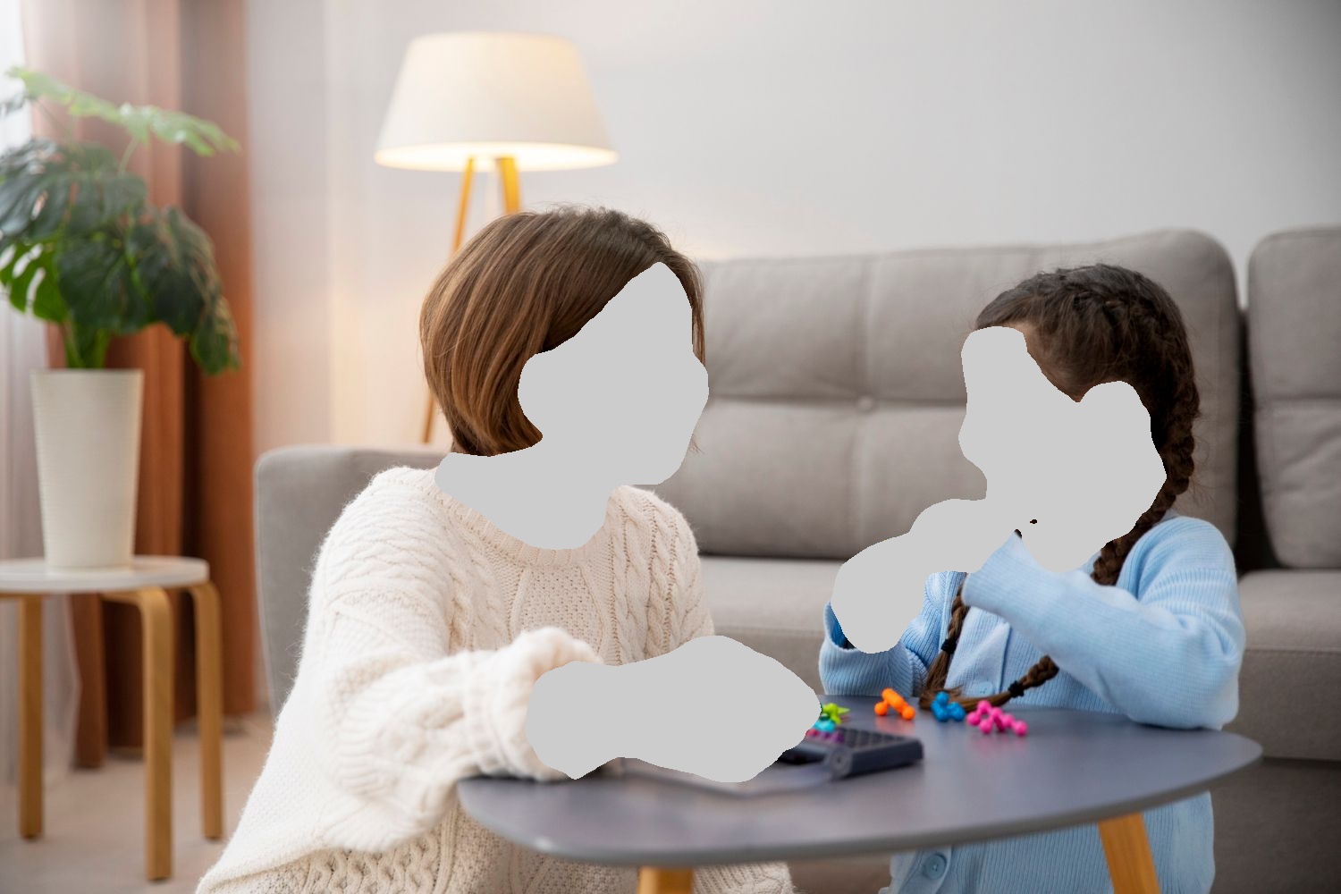 Woman and girl smiling, playing with toys at a table in a living room.