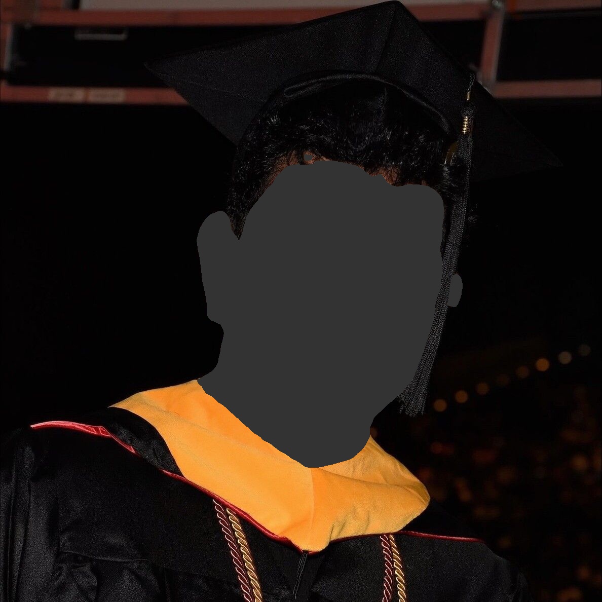 Person in graduation cap and gown, smiling slightly. Gold and black regalia, dark background.