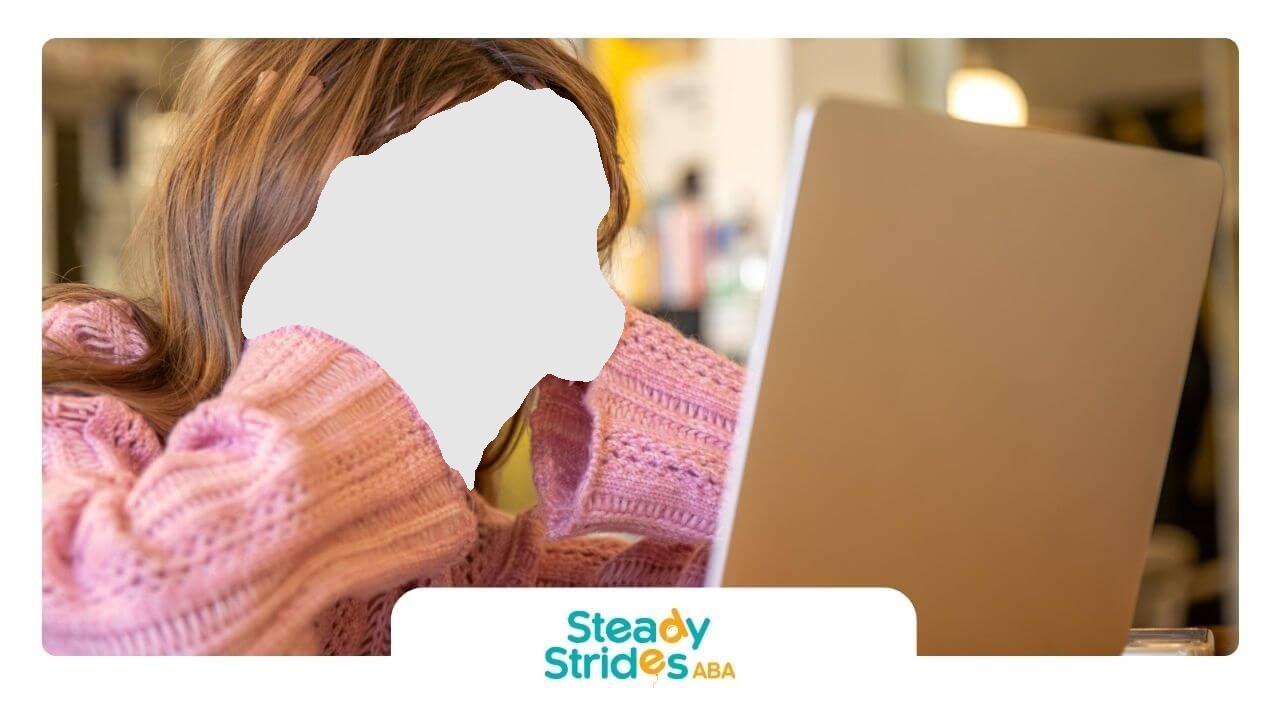 Girl with glasses looking frustrated at a laptop. Pink sweater, hands on head, indoor setting.