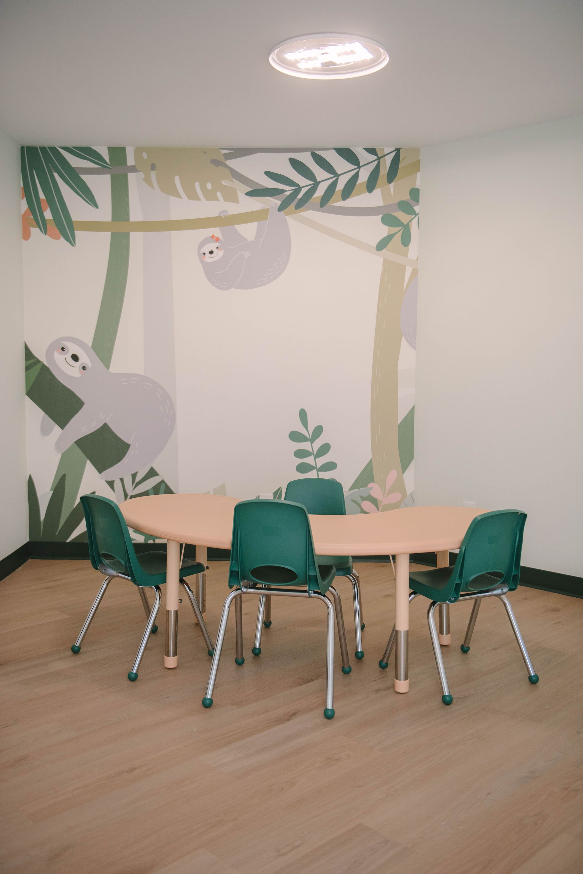 A room with a table and chairs and a painting of a sloth on the wall.