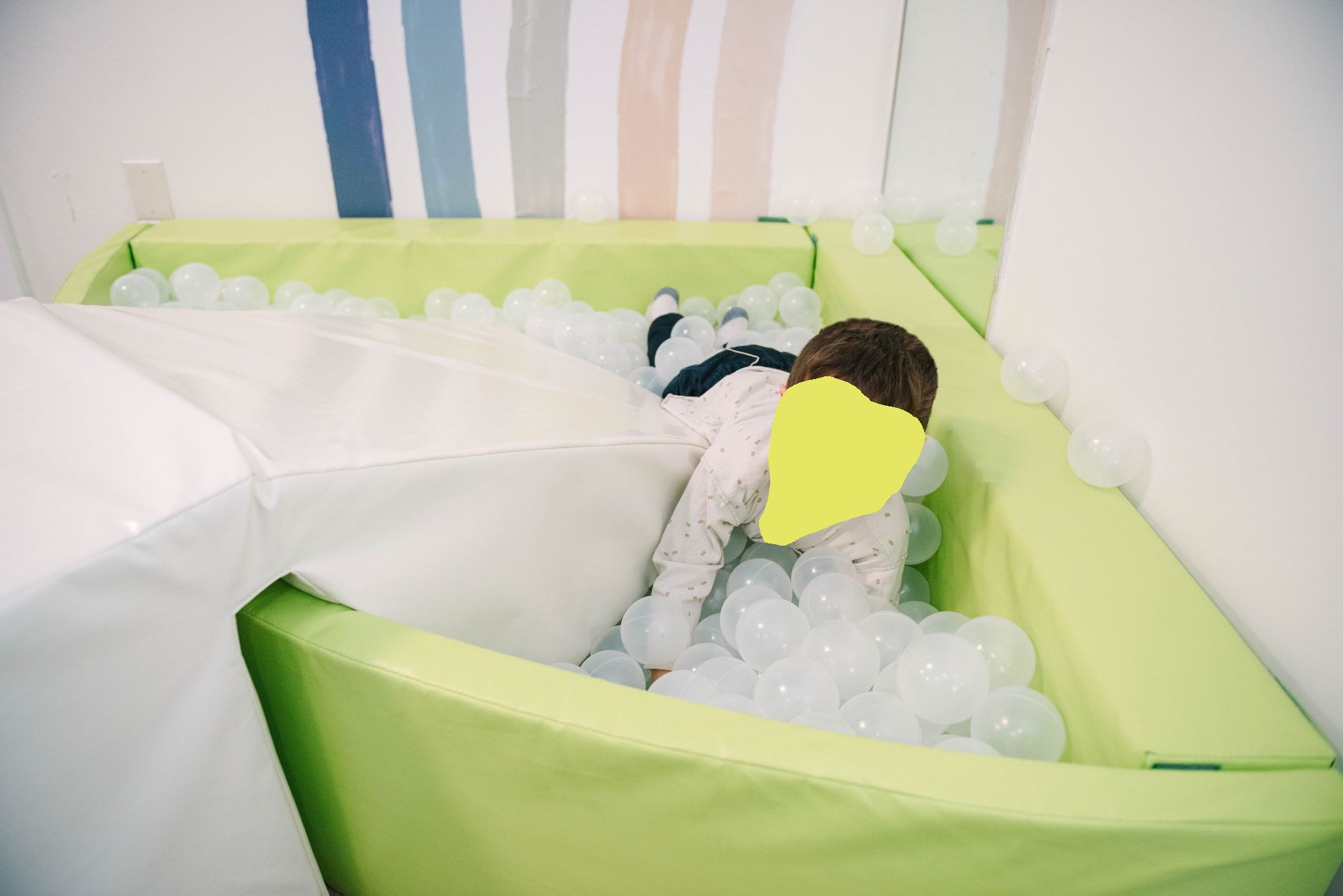 Boy smiles in a light green ball pit filled with white balls.