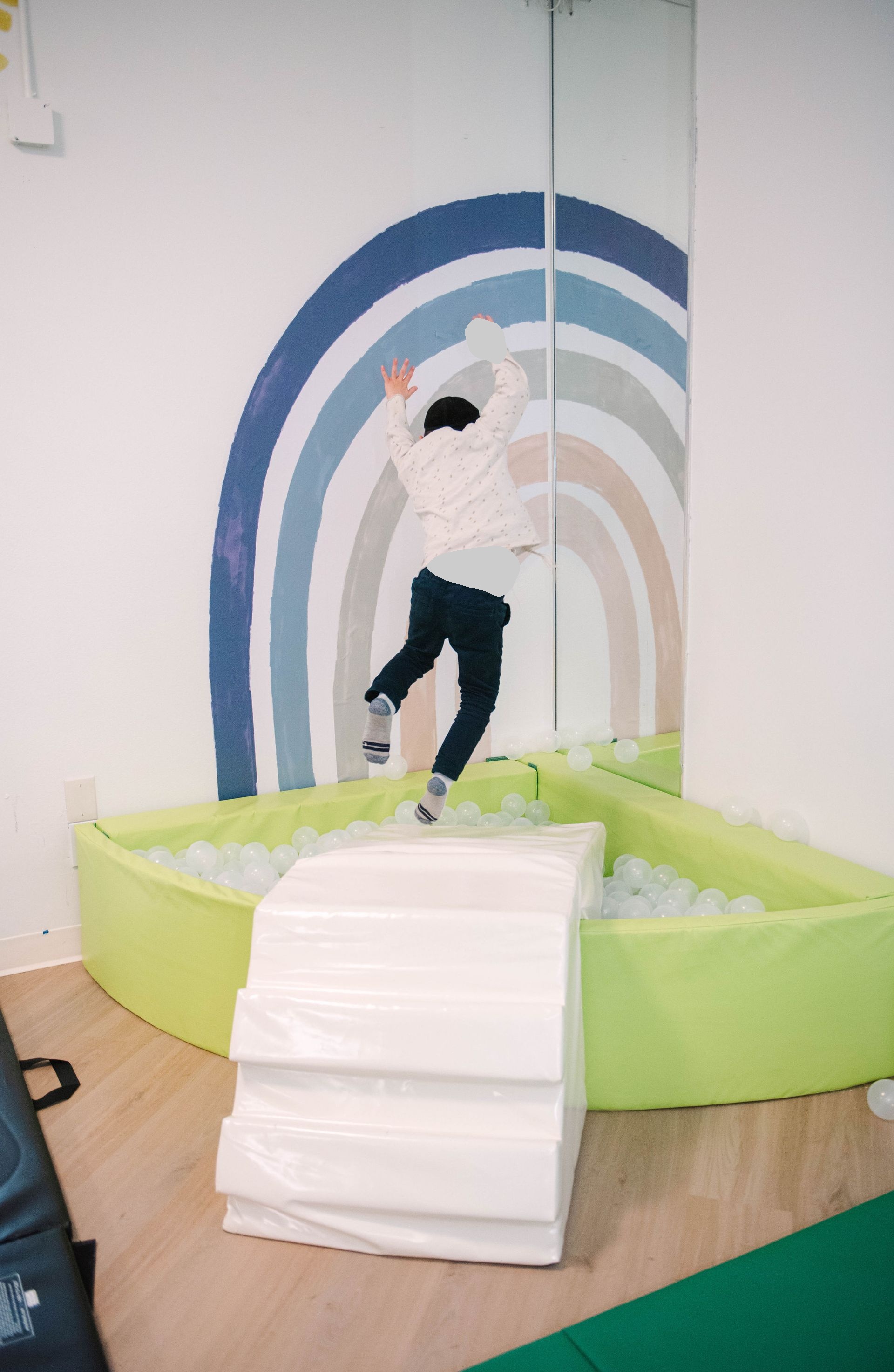 A child is jumping in a ball pit with a rainbow on the wall.
