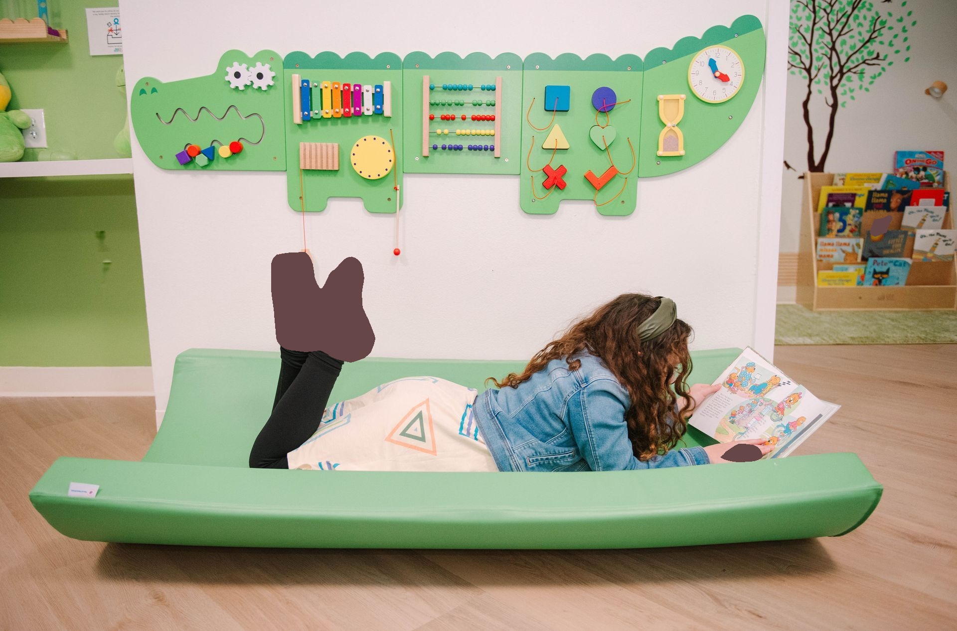 A little girl is laying on a green mat reading a book.