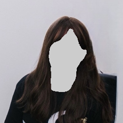 Woman with long brown hair, smiling, wearing a dark top, in front of a white wall.