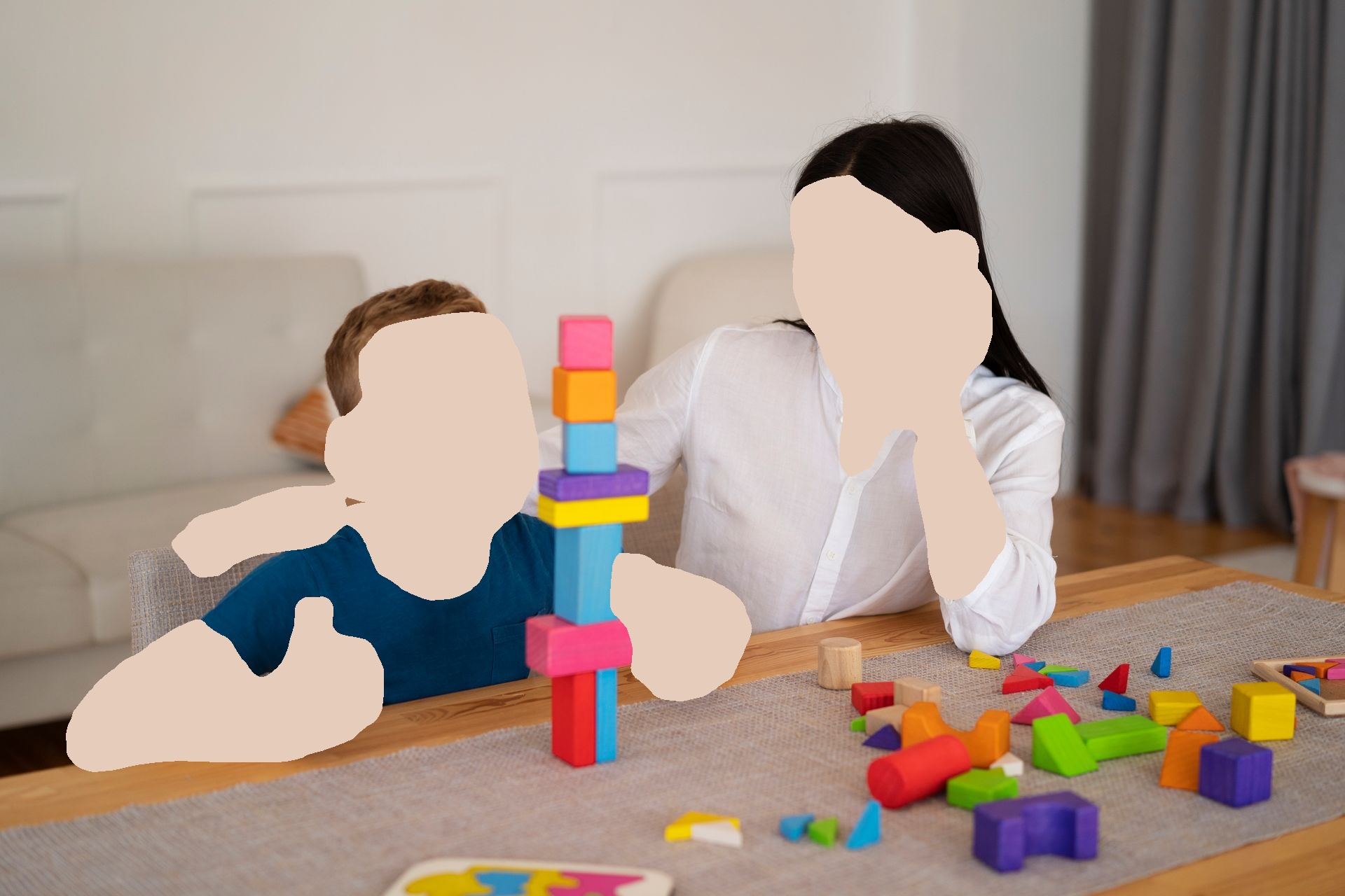 Woman and child building a tower of colorful blocks at a table. Child giving a thumbs up, smiling.