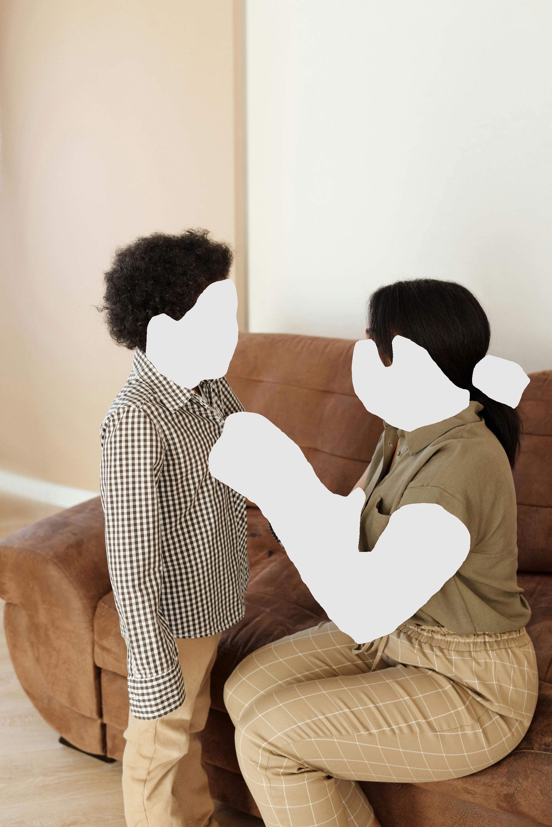 Woman buttoning a boy’s shirt. They are indoors by a brown couch.
