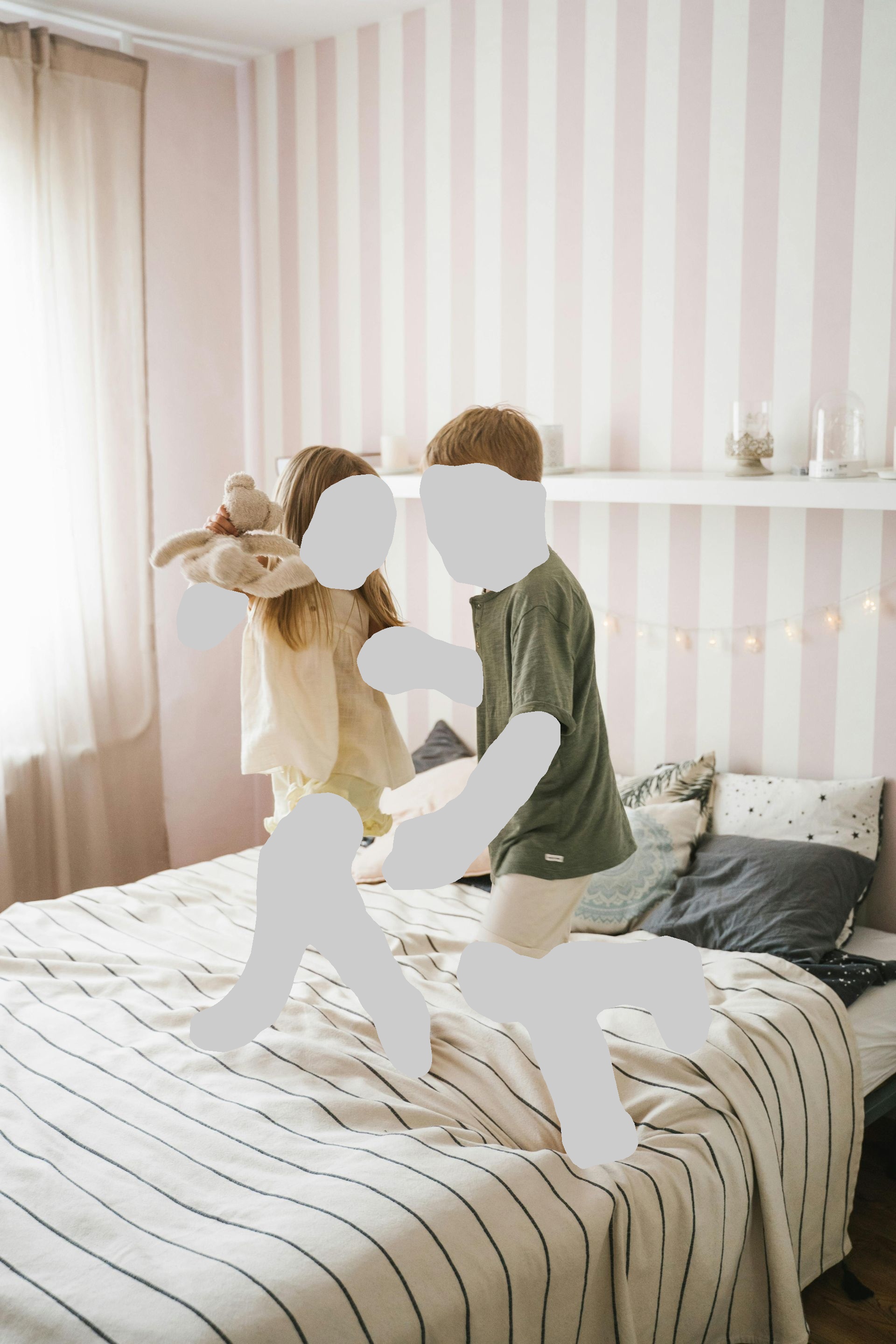 Two children jumping on a striped bed, laughing. Girl holds stuffed animal; boy wears green shirt and white shorts.