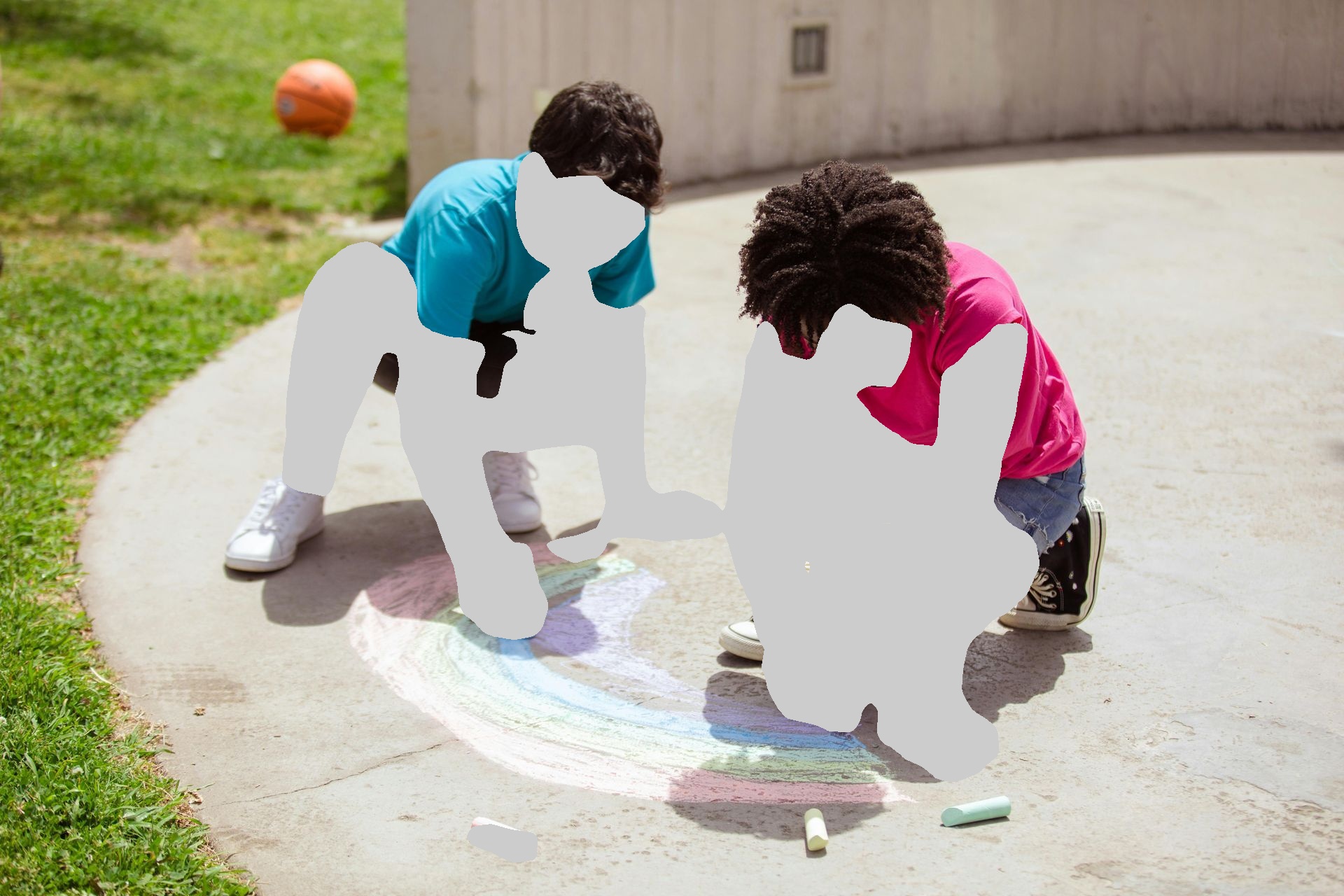 Two people crouched on a concrete surface, drawing a colorful rainbow with chalk outdoors; a basketball is in the background.