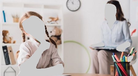 Girl with braids pondering at desk, therapist observing in background.